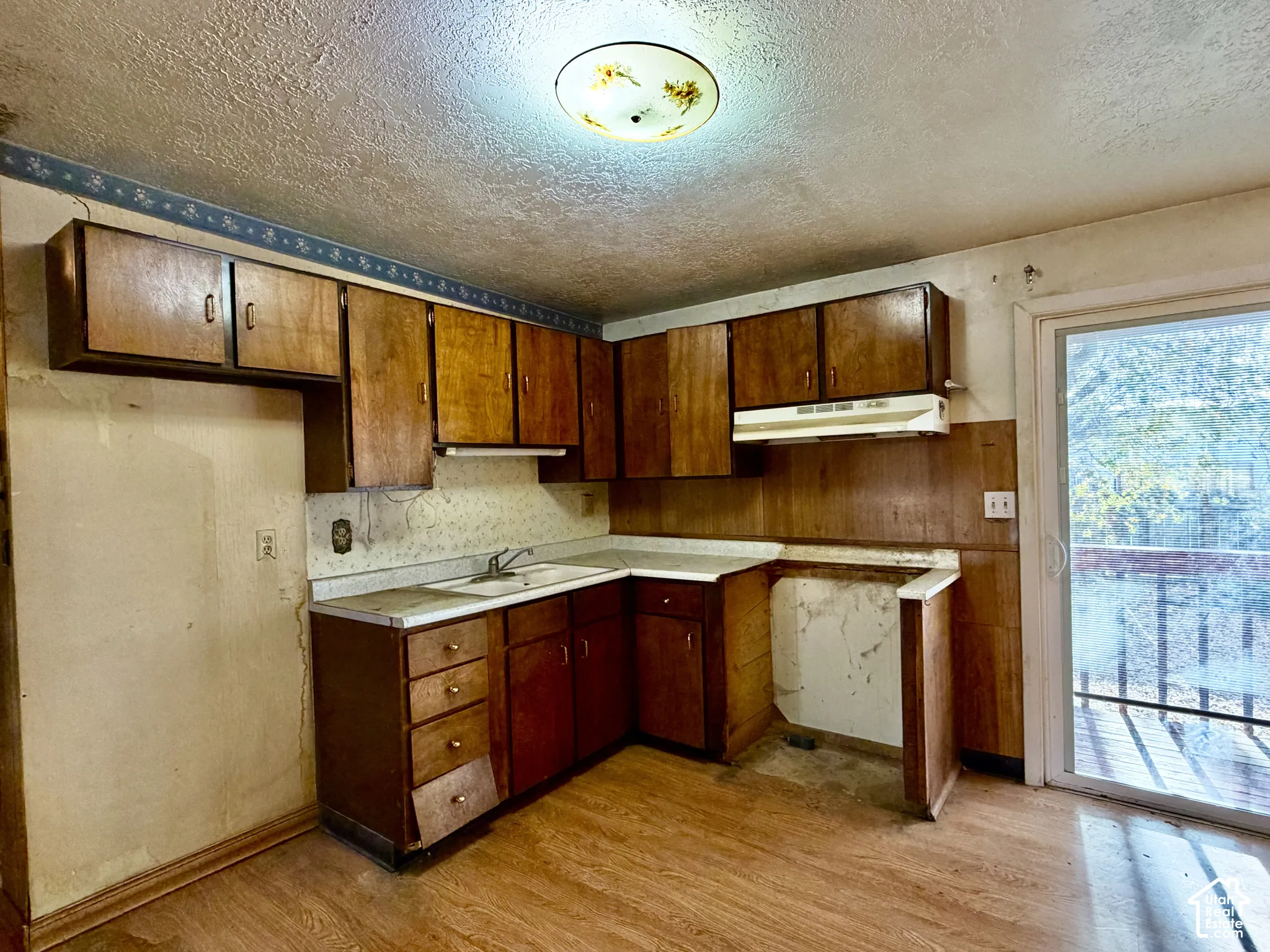 Kitchen featuring wood cabinetry, laminate countertops, integrated sink, overhead range hood, and glass sliding door