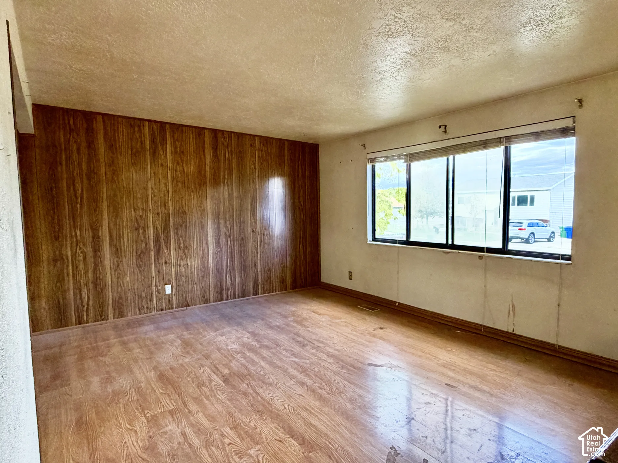Room interior featuring wood-finish flooring, wood-panel accent wall, and a large multi-pane window