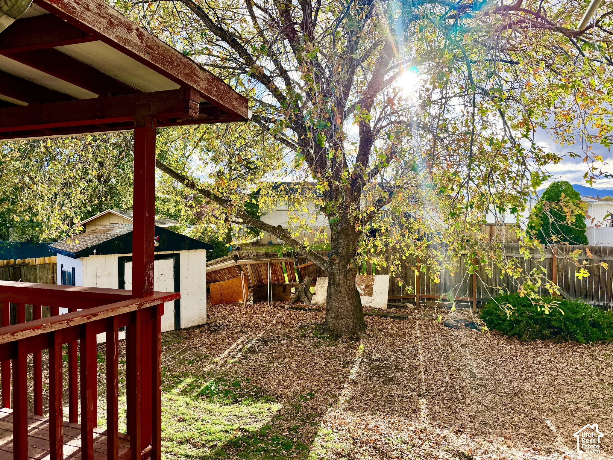 Outdoor space featuring a covered wooden deck, a mature tree, and a detached storage structure enclosed by perimeter fencing