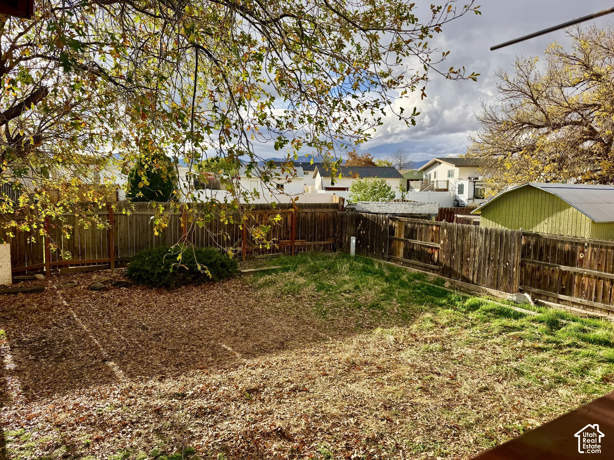 Backyard featuring perimeter wood fencing, mature trees, and a mountain backdrop