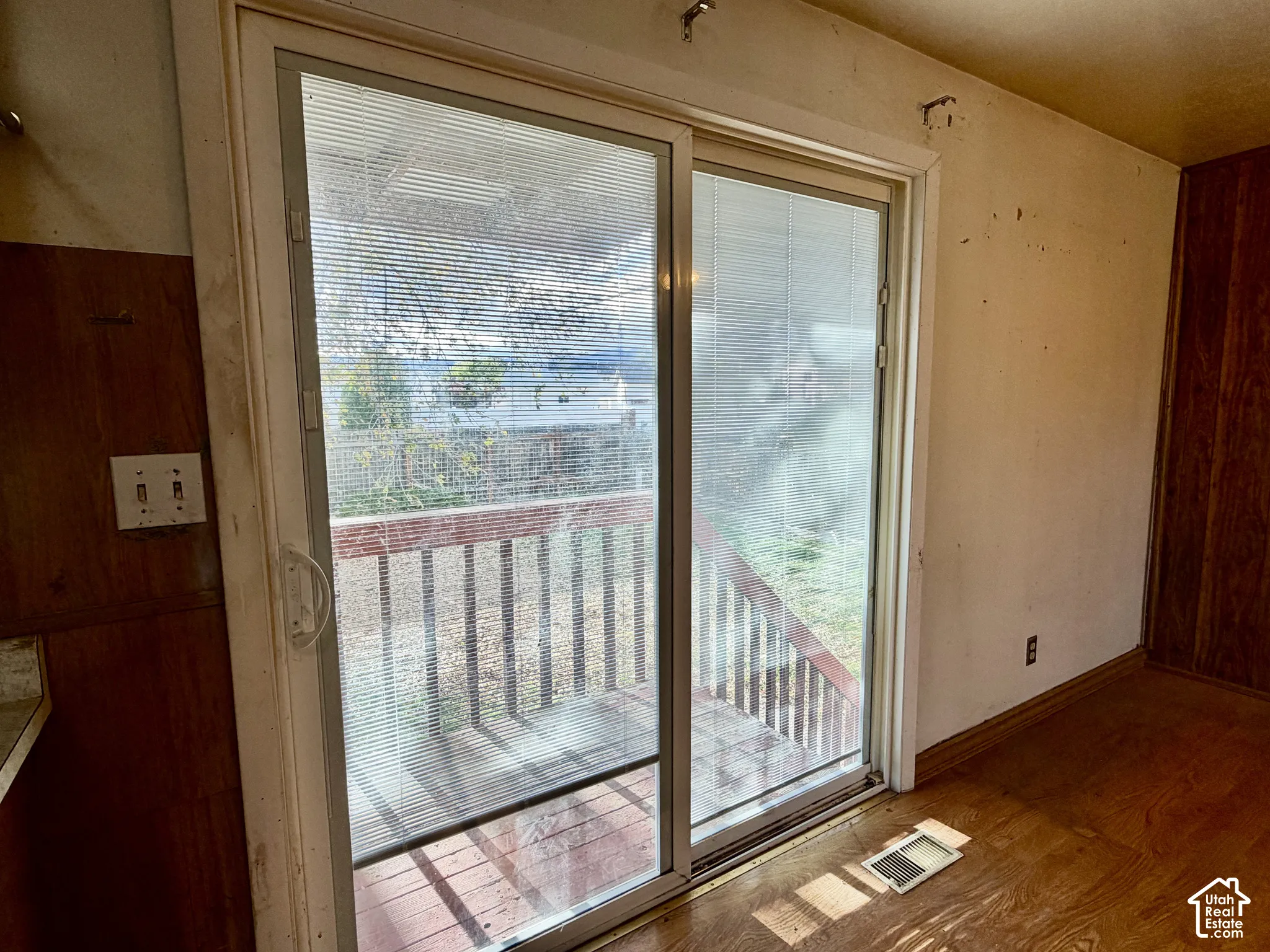 Sliding glass door with integrated blinds, wood-finish flooring, and exterior wooden deck