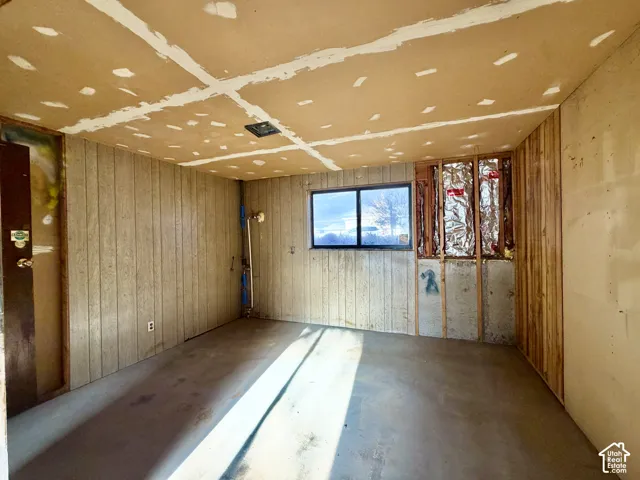 Interior room featuring vertical wood-paneled walls, concrete flooring, and a single-pane horizontal window