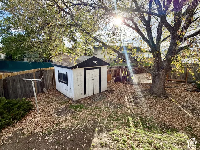 Storage shed with shingled roof, enclosed by wooden fencing and mature trees
