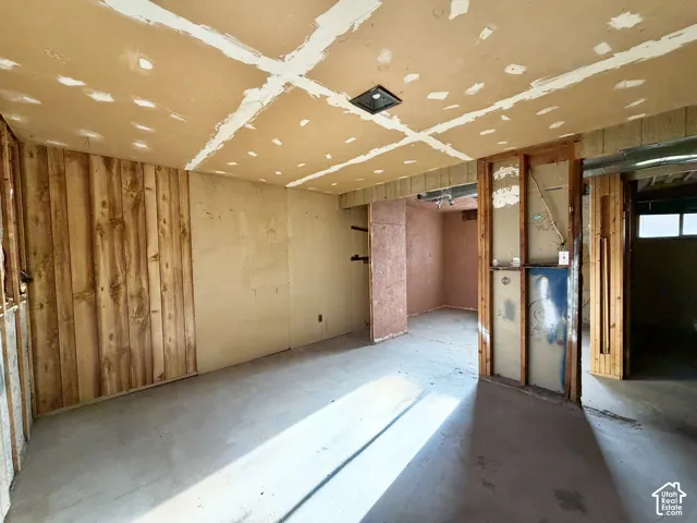 Open-concept interior space featuring exposed wood-stud framing, unfinished drywall surfaces, and vertical wood-finish paneling