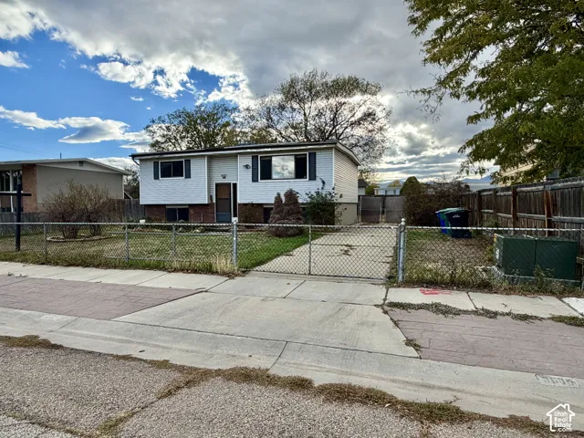 Single-story residence featuring light-toned horizontal siding, a brick lower-level exterior, a concrete driveway, and a chain-link fenced perimeter