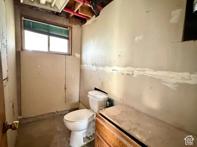 Single-story room featuring a window with a horizontal blind, a porcelain toilet, and wooden vanity cabinetry