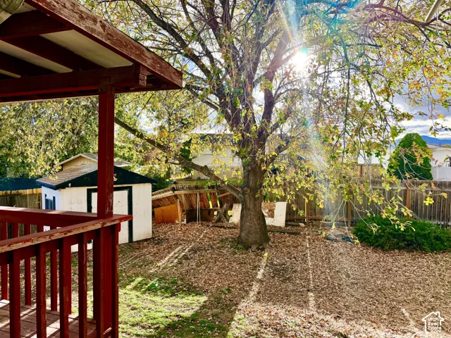 Outdoor space featuring a covered wooden deck, a mature tree, and a detached storage structure enclosed by perimeter fencing