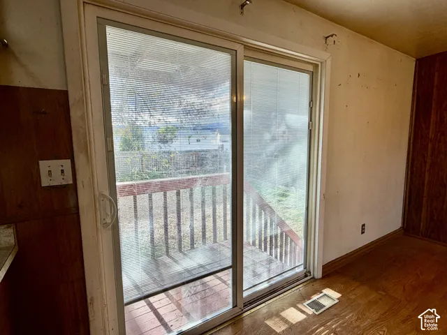 Sliding glass door with integrated blinds, wood-finish flooring, and exterior wooden deck