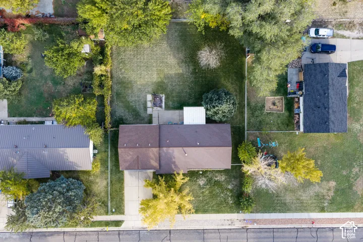 Aerial perspective of a property featuring a rectangular lot, a concrete driveway, a rear patio area, and mature trees