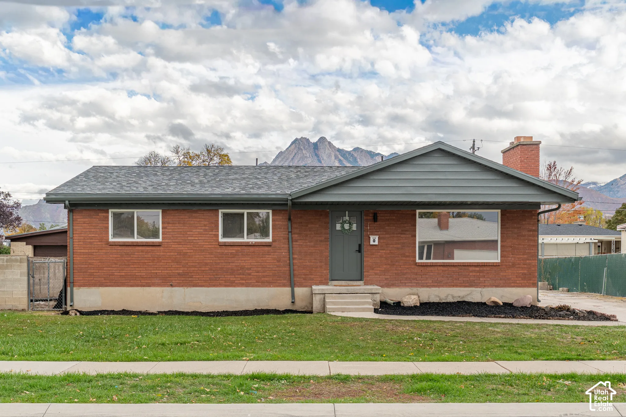 Single-story brick exterior featuring a red brick facade, gable roofline, exterior brick chimney, and prominent mountain backdrop