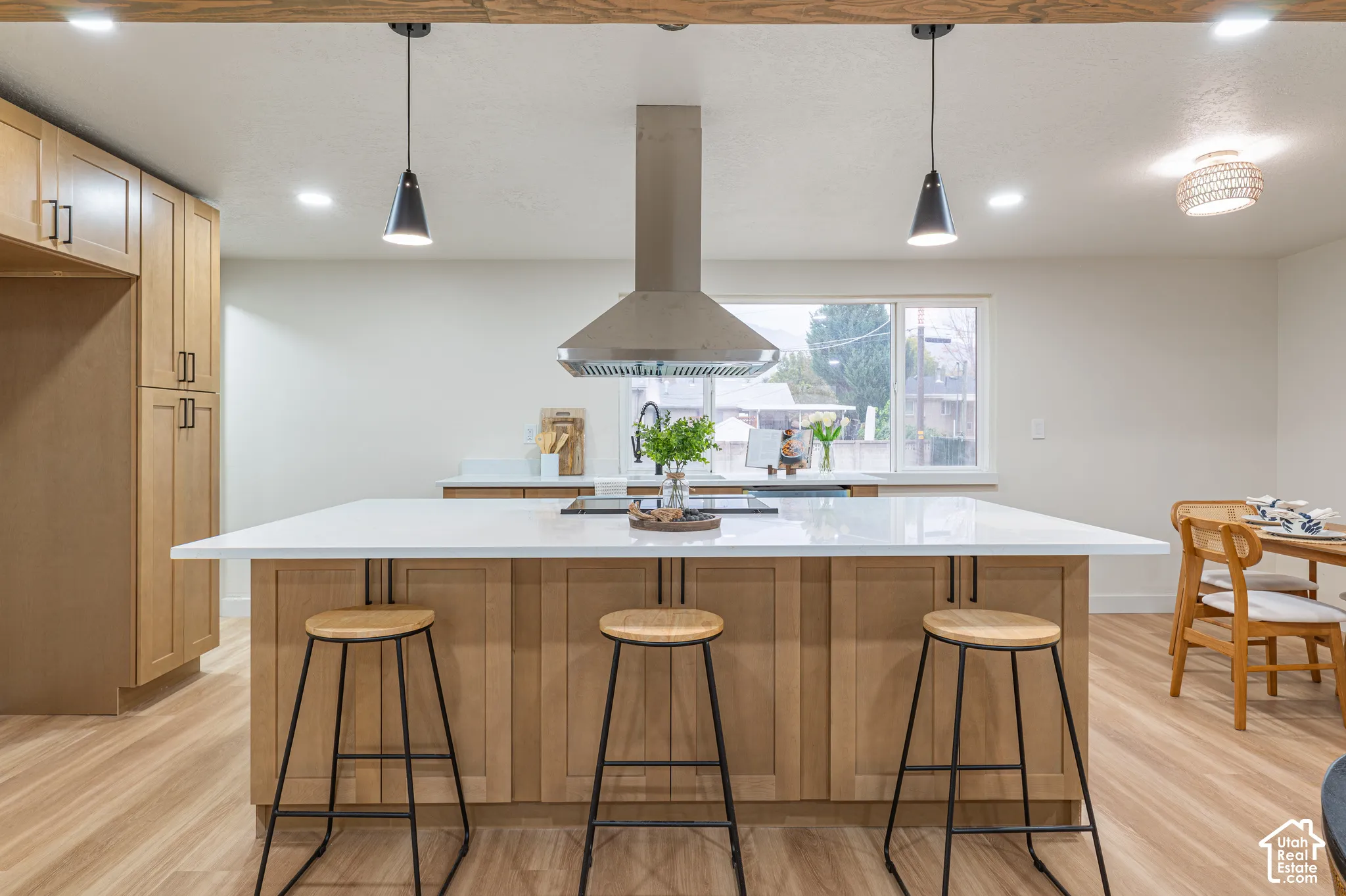 Kitchen featuring flat-panel wood cabinetry, a central island with a white countertop, recessed lighting, pendant fixtures, and a stainless steel range hood
