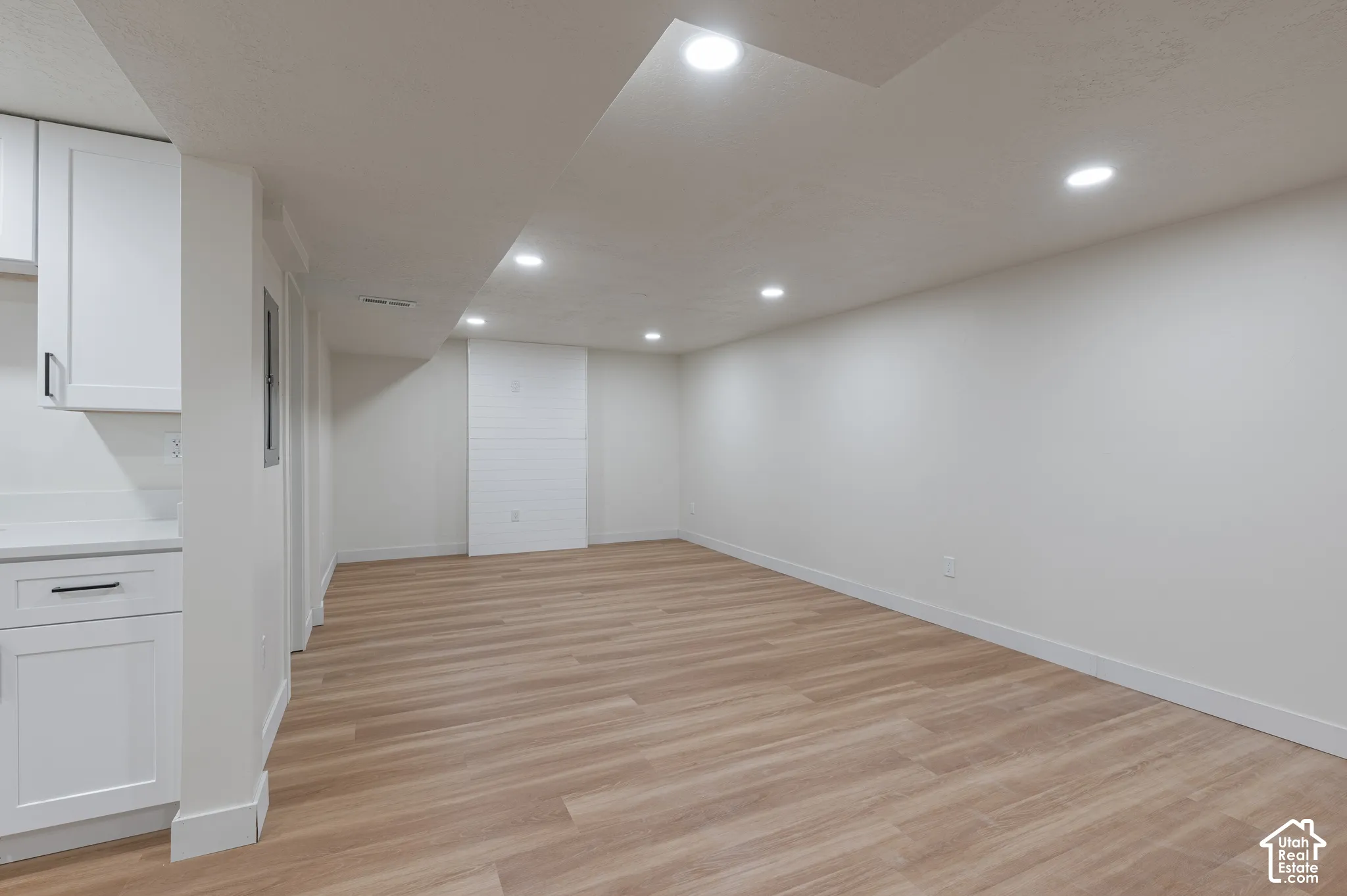 Open-concept room featuring wood-finish flooring, recessed lighting, white shaker-style cabinetry, and white shiplap accent wall detailing
