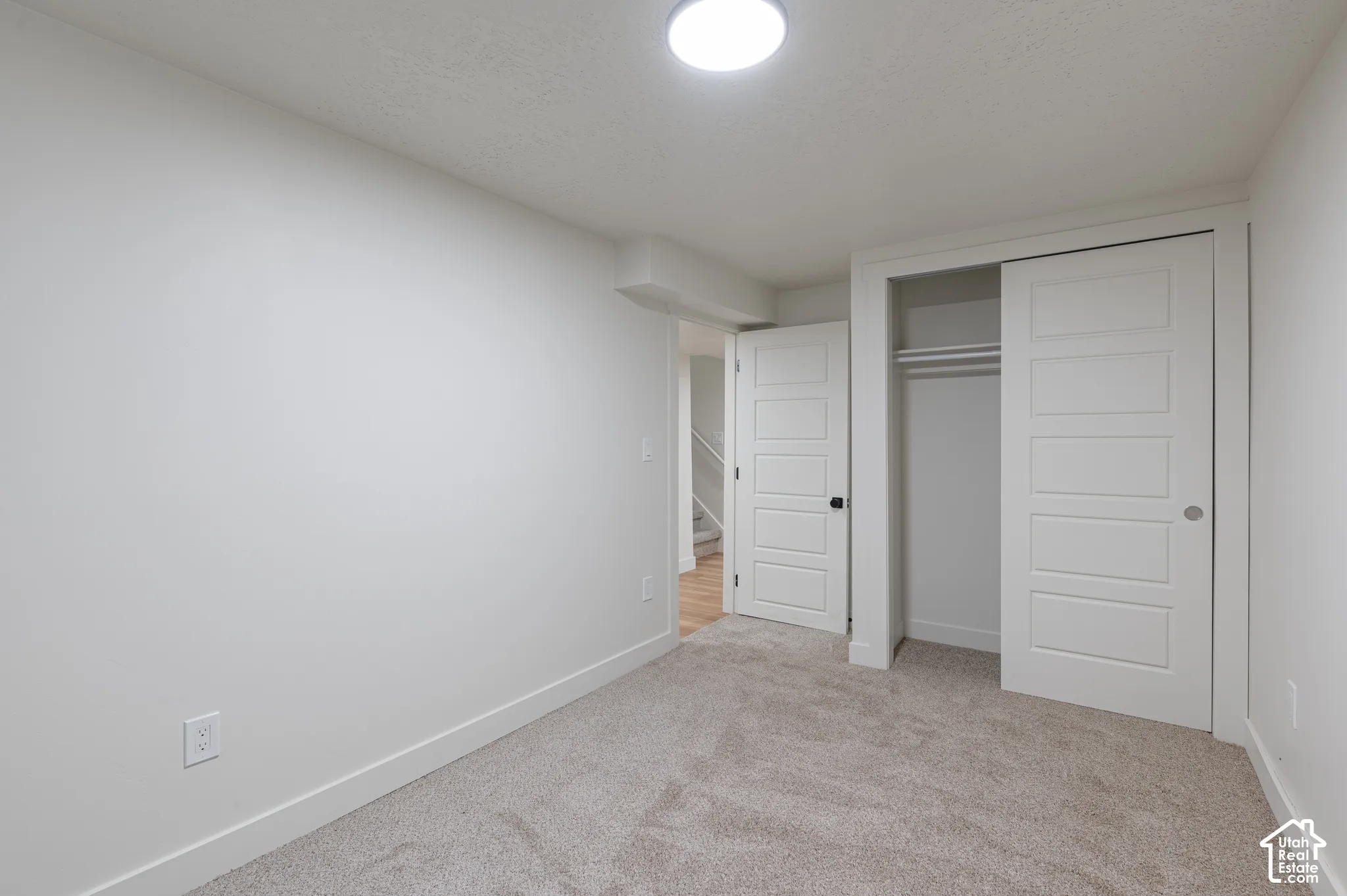 Neutral-toned room featuring fitted carpeting, a ceiling-mounted light fixture, a closet with sliding panel doors, and paneled interior doors
