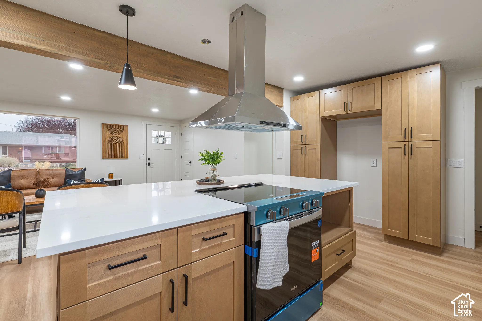 Kitchen featuring light wood-finish cabinetry, quartz countertops, a stainless steel range with overhead chimney hood, and a decorative exposed wood beam