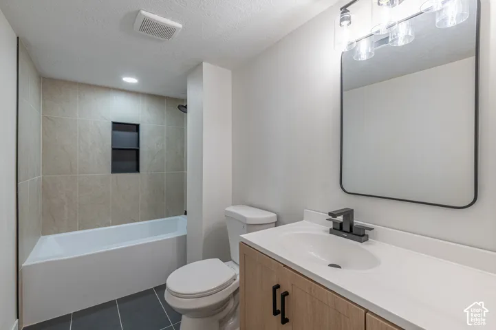 Bathroom featuring a wood-finish vanity with matte black hardware, integrated white countertop sink, rectangular wall-mounted mirror, and a tile-surround bathtub with a built-in recessed niche