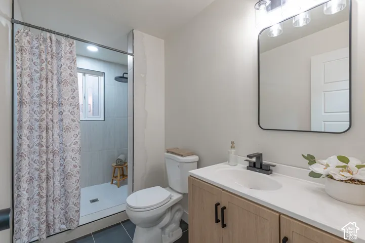 Bathroom featuring a wood-finish vanity with a light-toned countertop, rectangular wall-mounted mirror, matte black faucet and cabinet hardware, and a walk-in shower with full-height tile surround