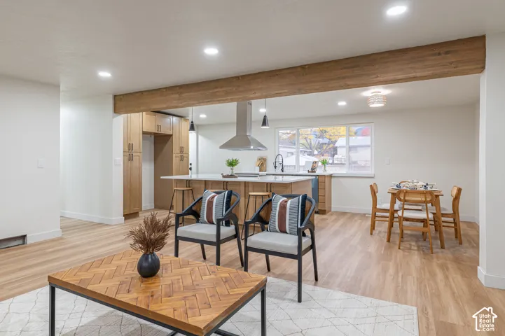 Kitchen featuring light wood cabinetry, a central island with a countertop, stainless steel range hood, recessed lighting, and wood-finish flooring with an exposed structural beam