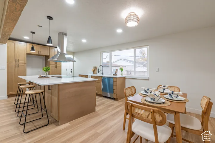 Kitchen featuring wood-finish cabinetry, a central island with a stone-surface countertop, stainless steel chimney-style range hood, wood-finish flooring, and recessed lighting