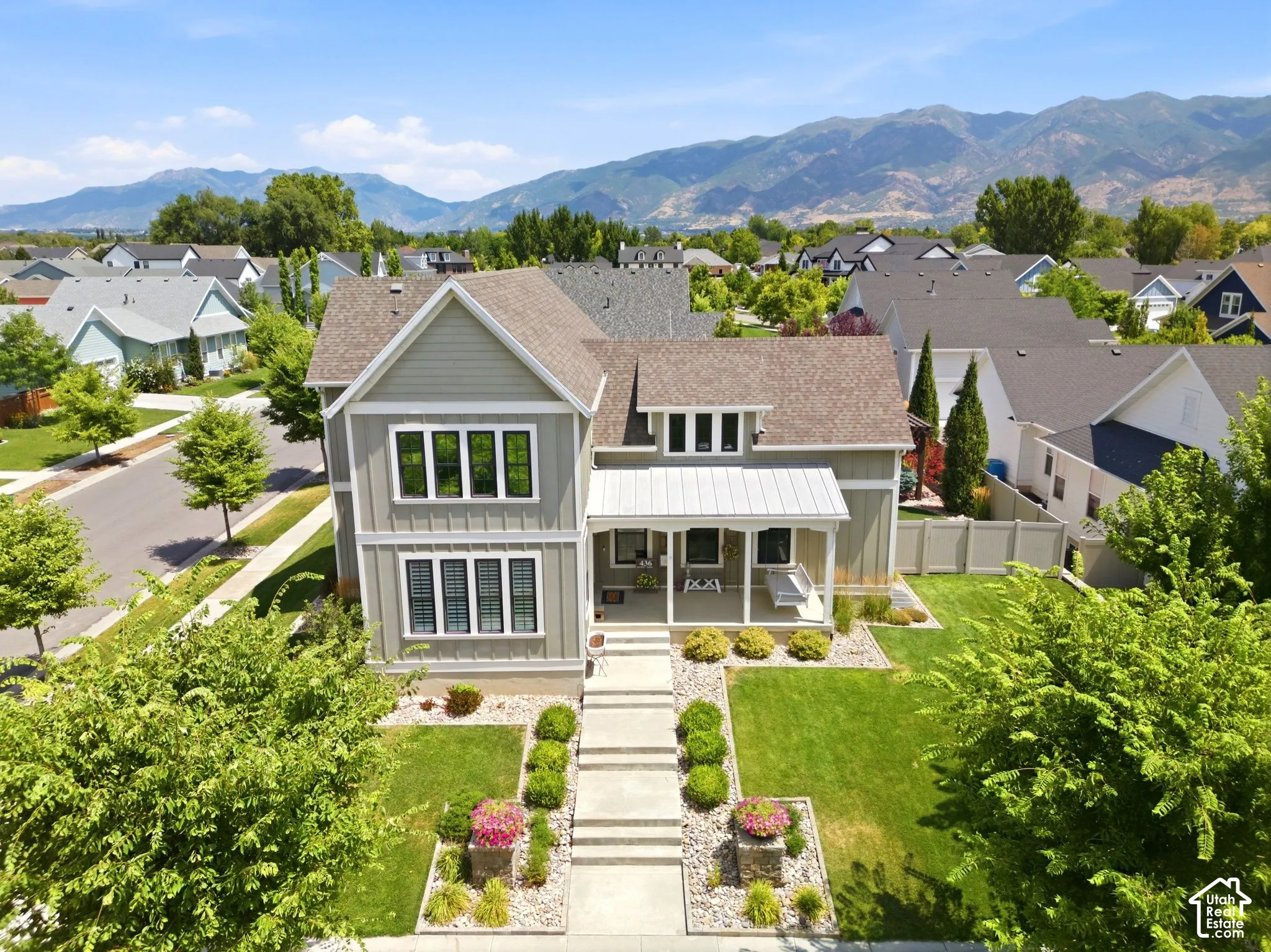 Two-story home exterior featuring vertical lap siding, a metal-roofed covered front porch, tiered concrete steps, landscaped garden beds with stone borders, and mountain backdrop