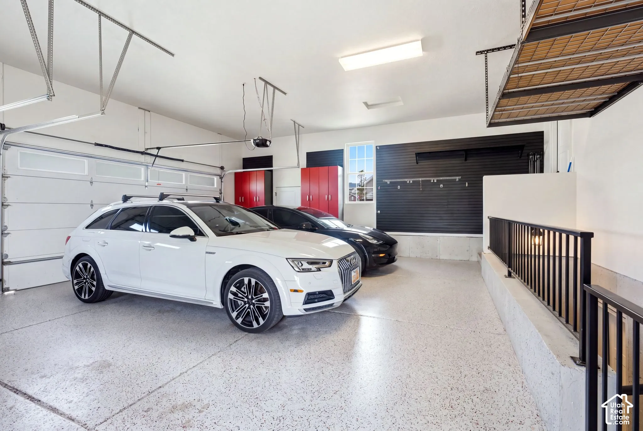3-car garage featuring epoxy-coated flooring, wall-mounted storage panels, built-in red cabinetry, and overhead hanging rack