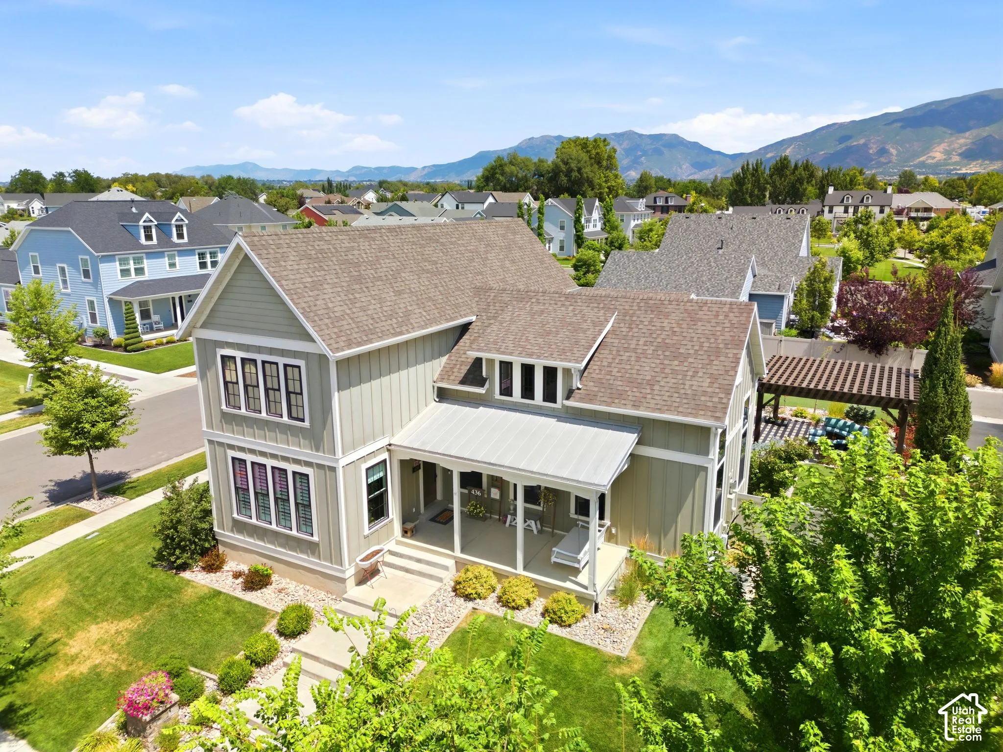 Two-story residence featuring vertical siding, a covered front porch with a metal roof, a composite shingle roof, and a backyard pergola against a mountain backdrop