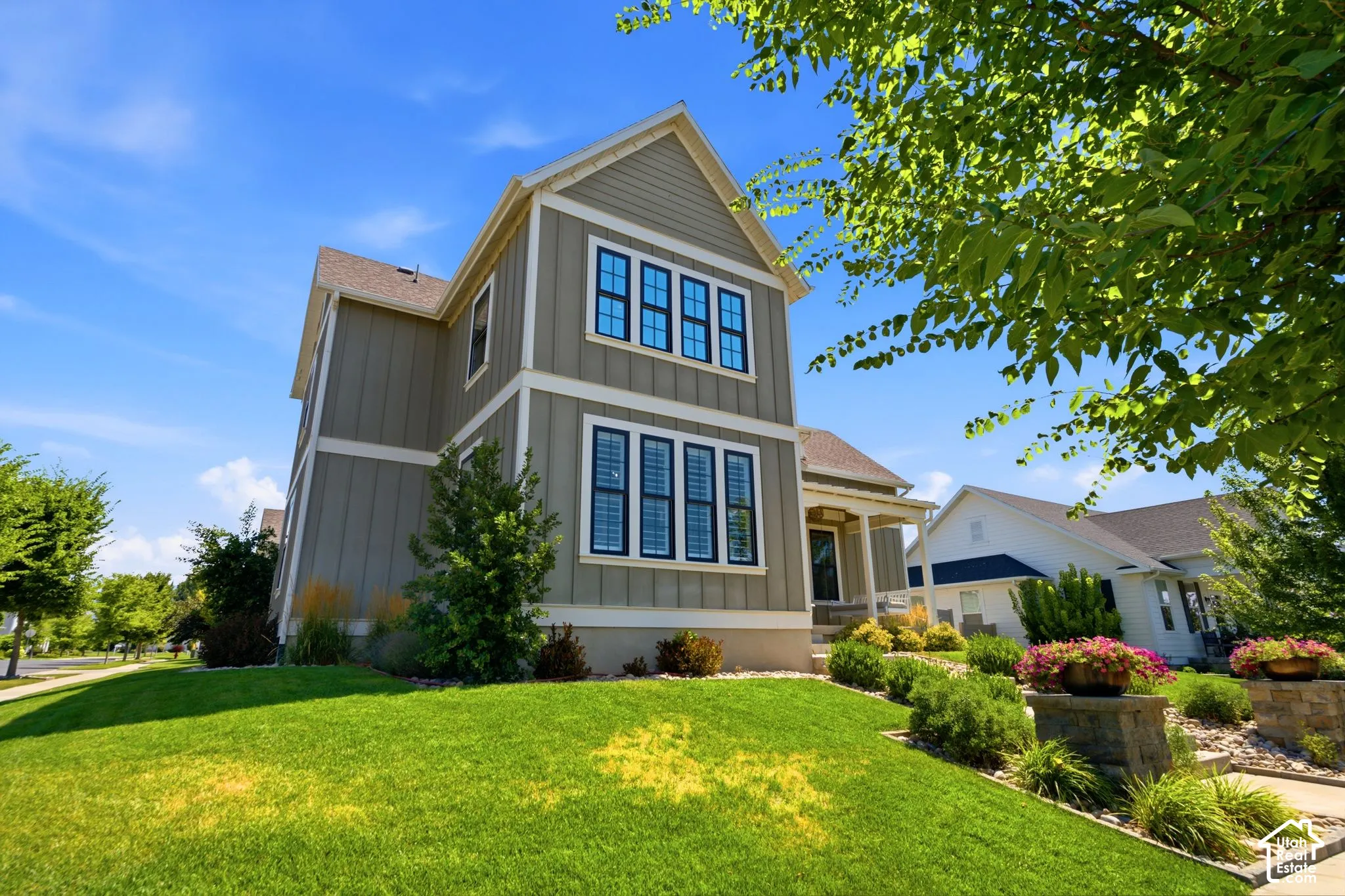 Two-story exterior featuring vertical siding, multi-pane windows with dark trim, a covered front porch, and manicured landscaping with stone-accented garden beds