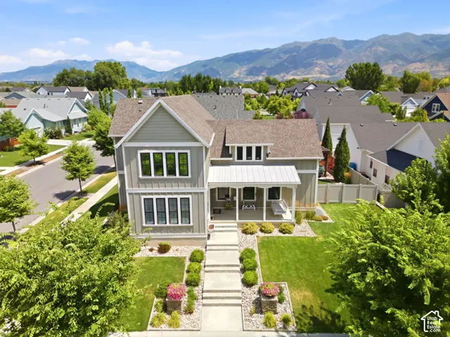 Two-story home exterior featuring vertical lap siding, a metal-roofed covered front porch, tiered concrete steps, landscaped garden beds with stone borders, and mountain backdrop