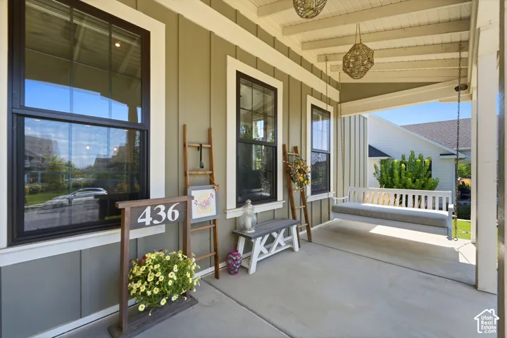 Covered front porch featuring board-and-batten siding, oversized windows with dark frames, a bead-board ceiling, and cozy porch swing