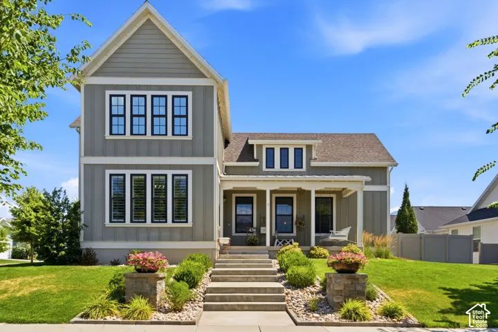 Two-story residence featuring vertical board-and-batten siding, multi-pane windows with dark trim, a covered front porch, and stone-accented concrete entry steps