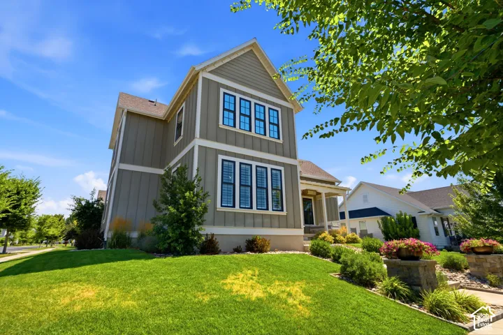 Two-story exterior featuring vertical siding, multi-pane windows with dark trim, a covered front porch, and manicured landscaping with stone-accented garden beds