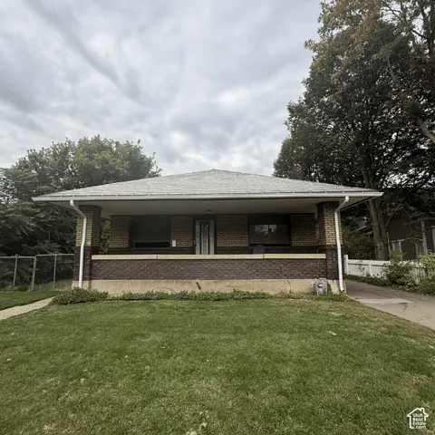 Single-story exterior featuring multi-toned brick masonry, a hipped roof, and a covered front porch with brick pillars