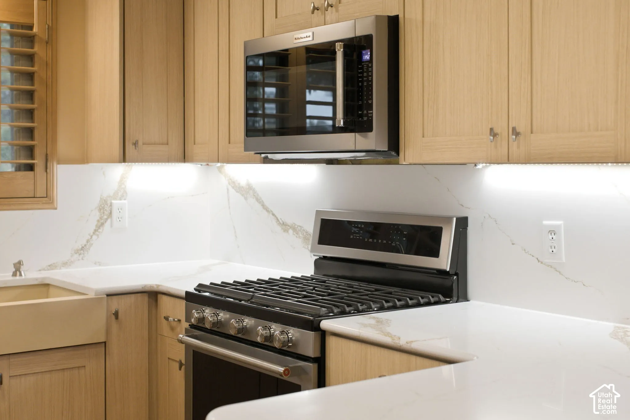 Light wood cabinetry, stainless steel gas range, built-in stainless steel microwave, stone-finish countertops, and integrated under-cabinet lighting