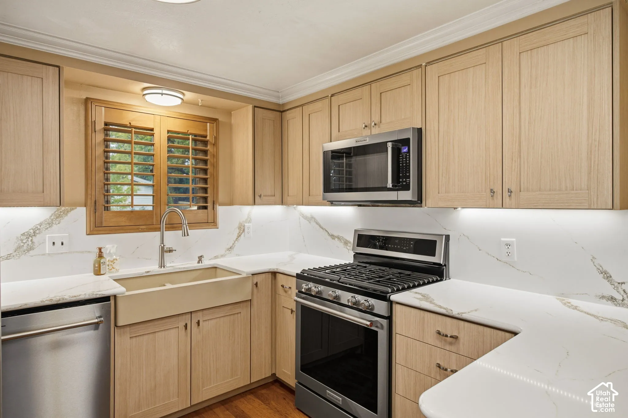 Kitchen featuring light-finish cabinetry, solid-surface countertops with stone-pattern veining, a farmhouse-style sink, stainless steel appliances, and wood-finish flooring