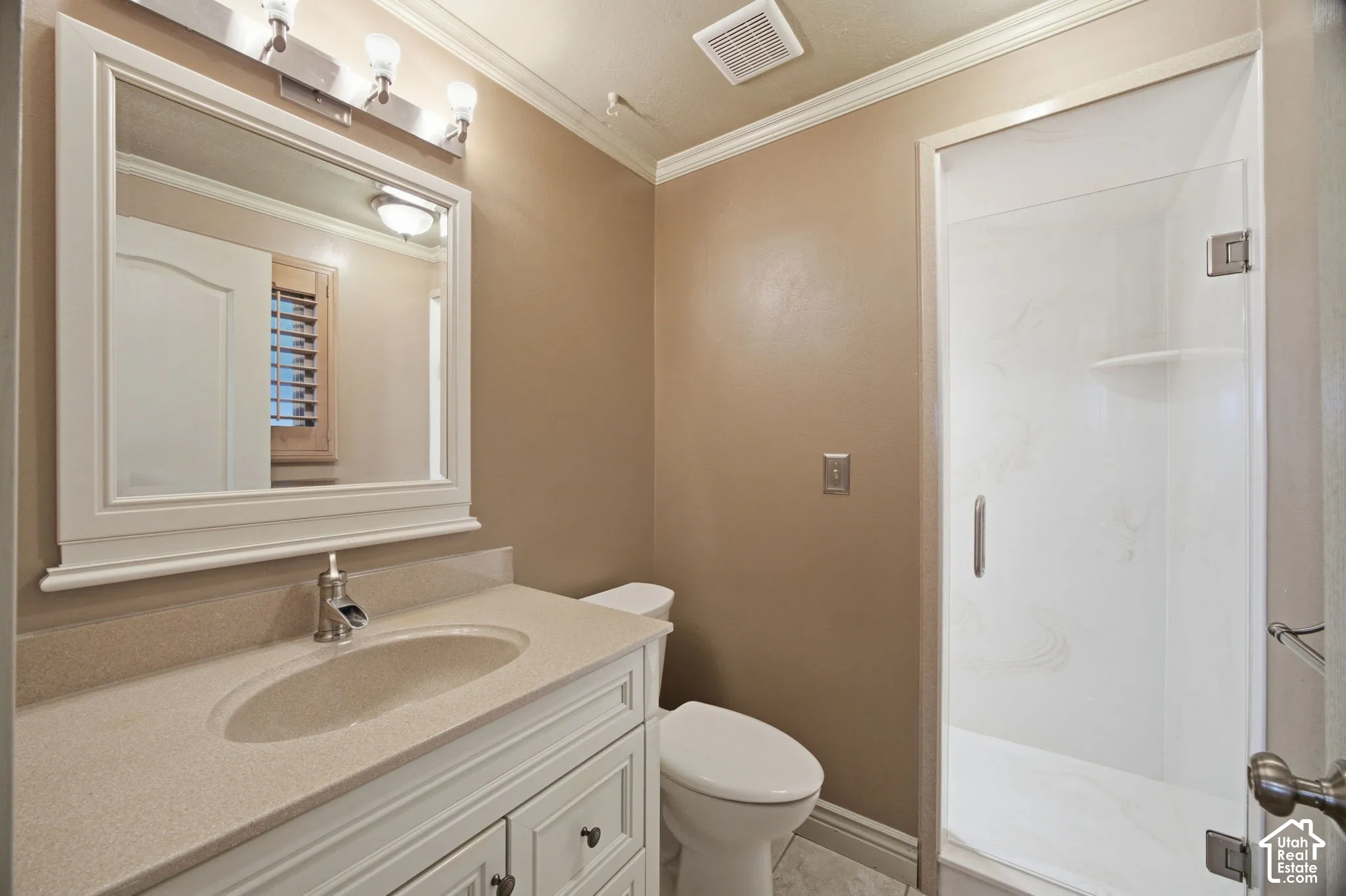 Primary Bathroom featuring a white vanity with a composite countertop and integrated sink, a framed wall mirror with multi-light fixture, and a glass-enclosed shower with tiled surround