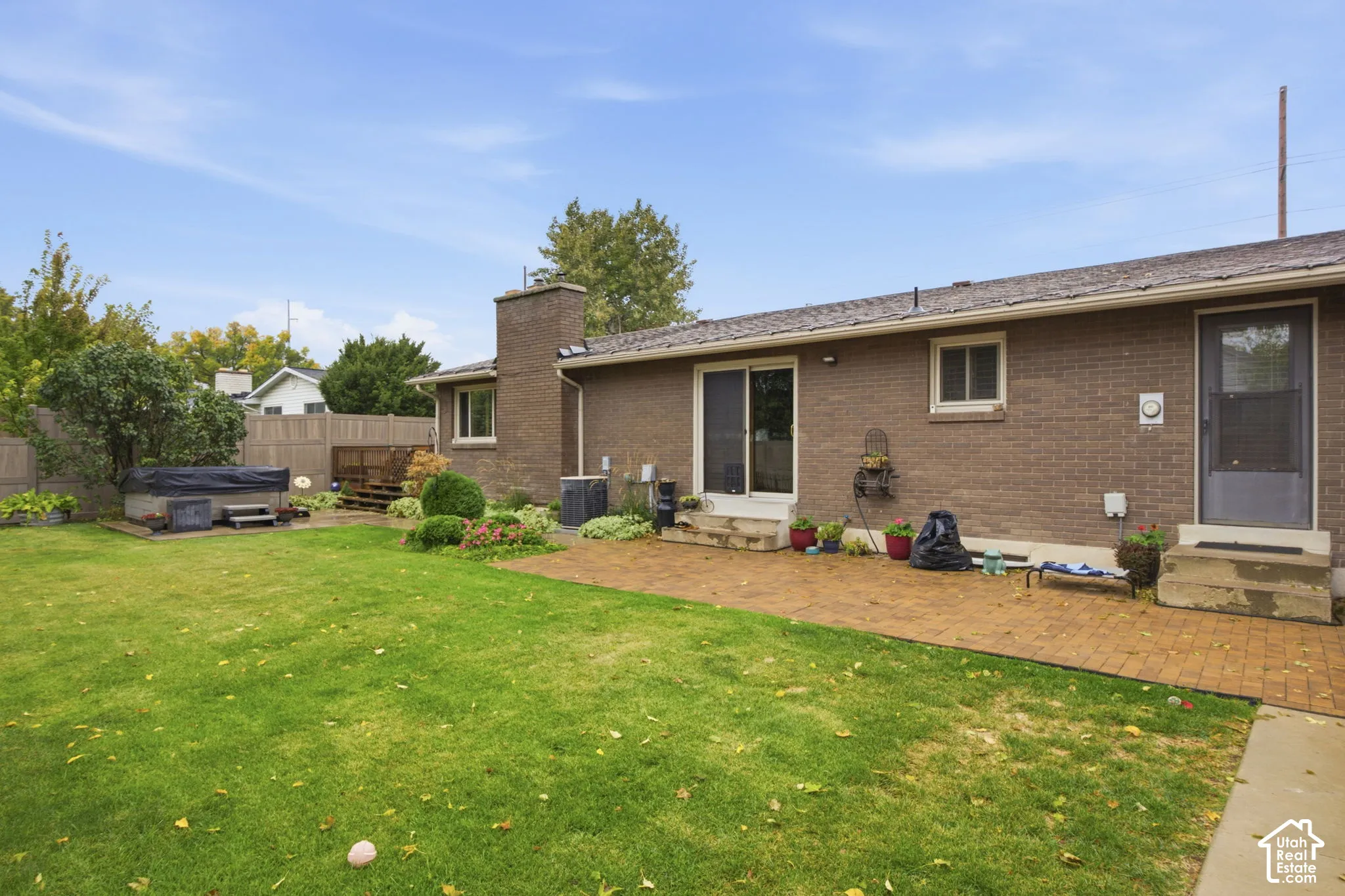 Brick exterior with masonry chimney, paver patio, wood-finish privacy fencing, and expansive lawn
