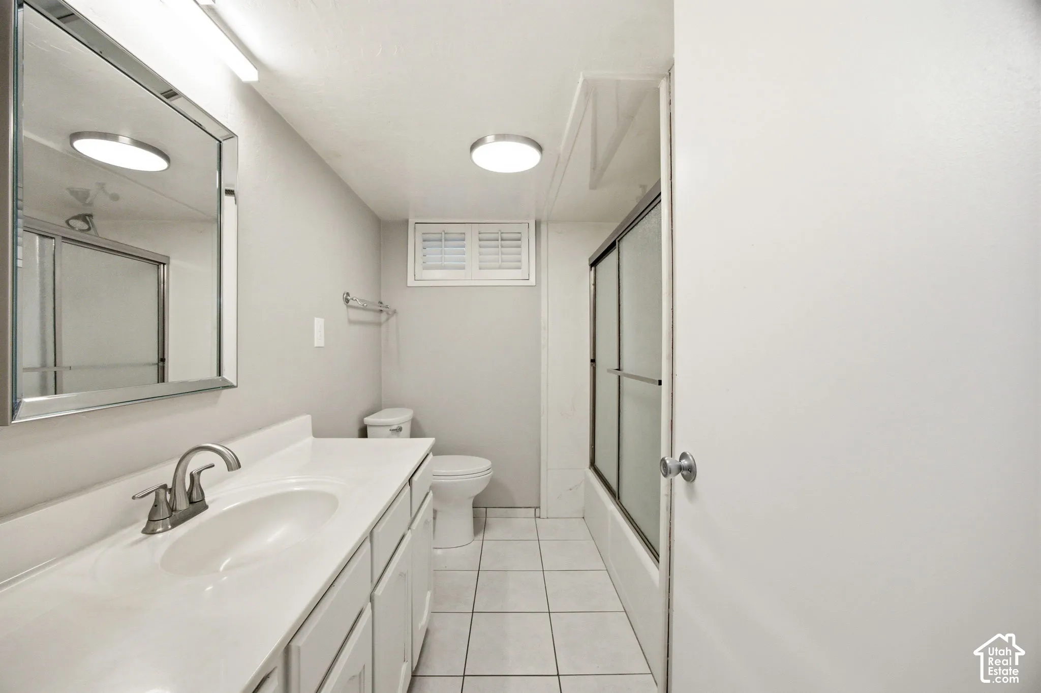 Bathroom featuring a white vanity with an integrated sink, polished chrome faucet, rectangular wall-mounted mirror, and tile flooring
