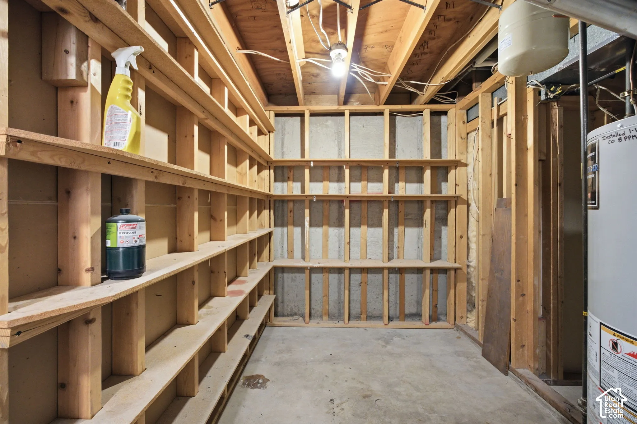 Unfinished lower level space featuring exposed wood-stud framing, concrete foundation walls, built-in wooden shelving, and a concrete floor