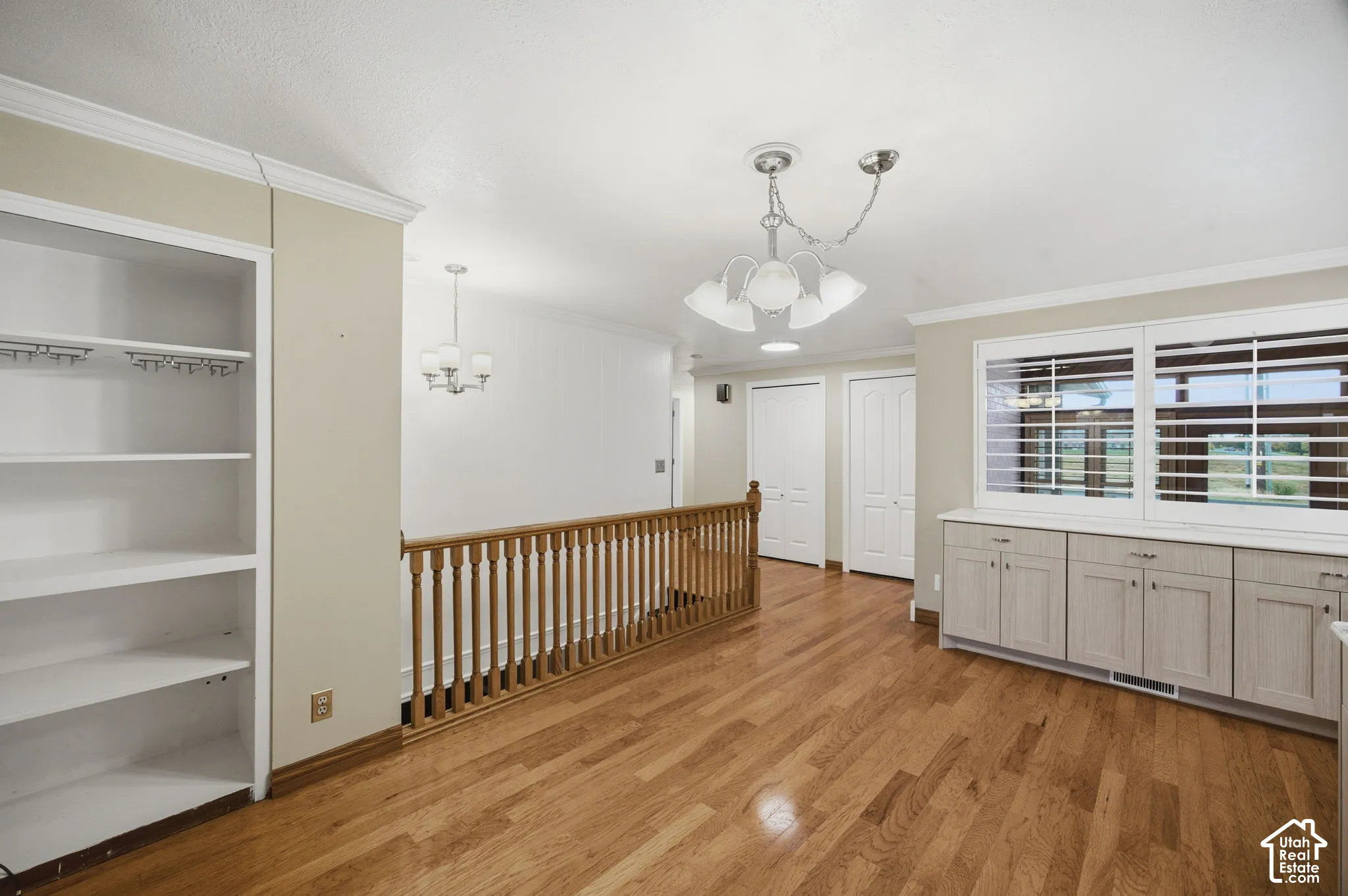 Interior space featuring wood-finish flooring, white built-in shelving, custom cabinetry with a solid surface countertop, louvered window shutters, and wood-railing staircase balustrade