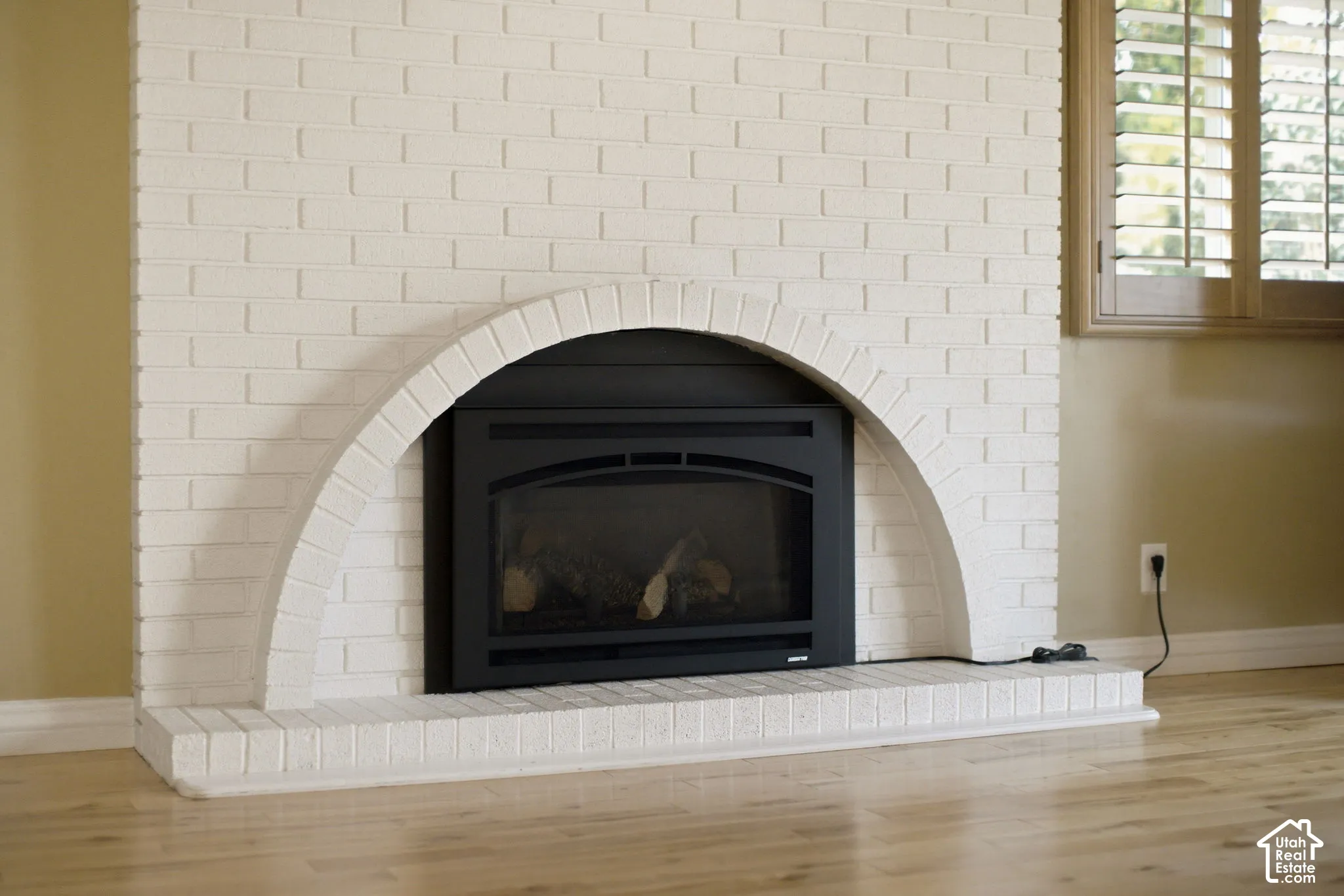 Fireplace featuring a white-painted brick surround, arched masonry detail, black metal firebox insert, and wood-finish flooring