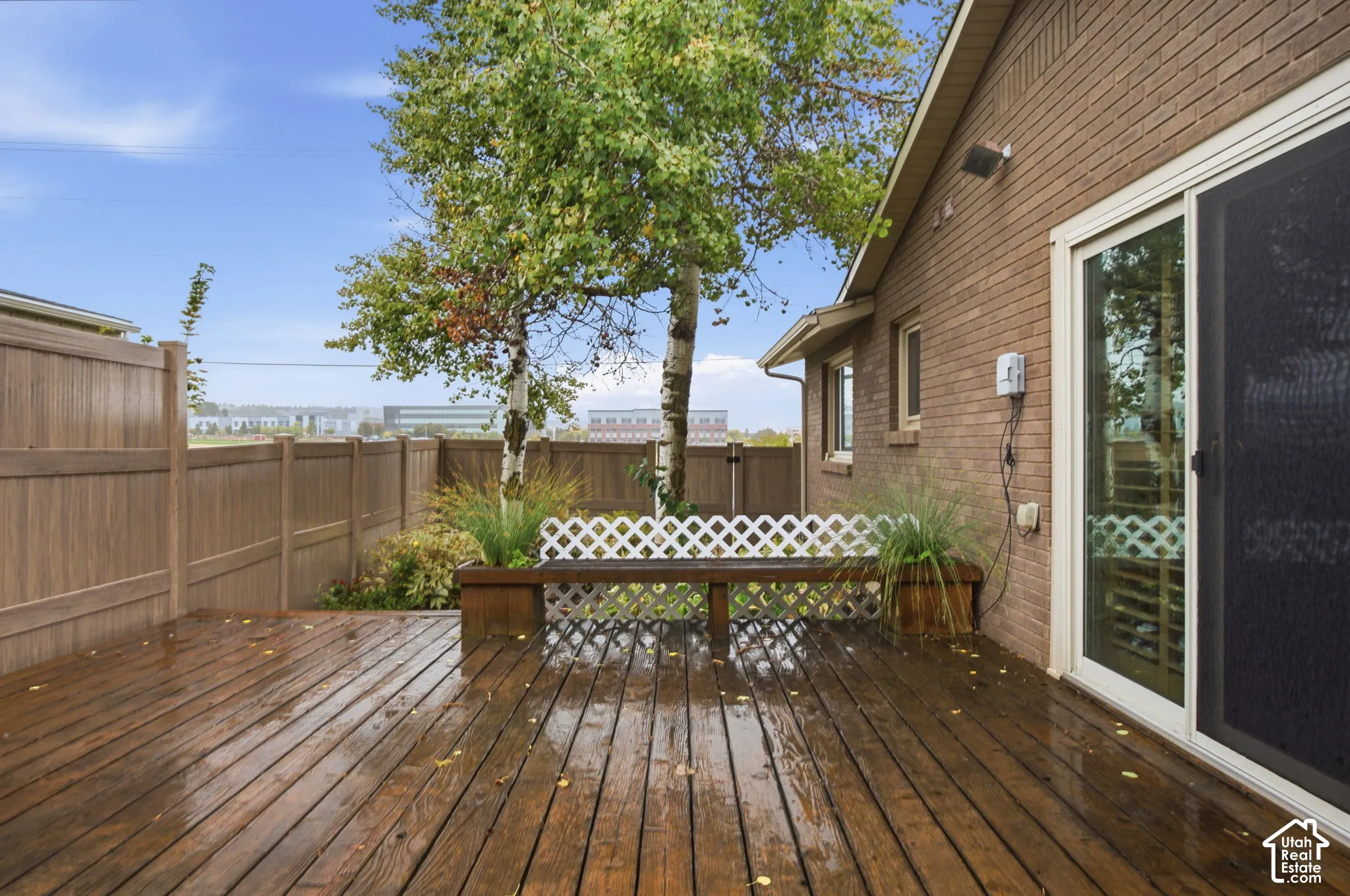 Wood-deck patio featuring a brick exterior wall, solid-panel perimeter fencing, built-in wooden bench, and lattice detailing