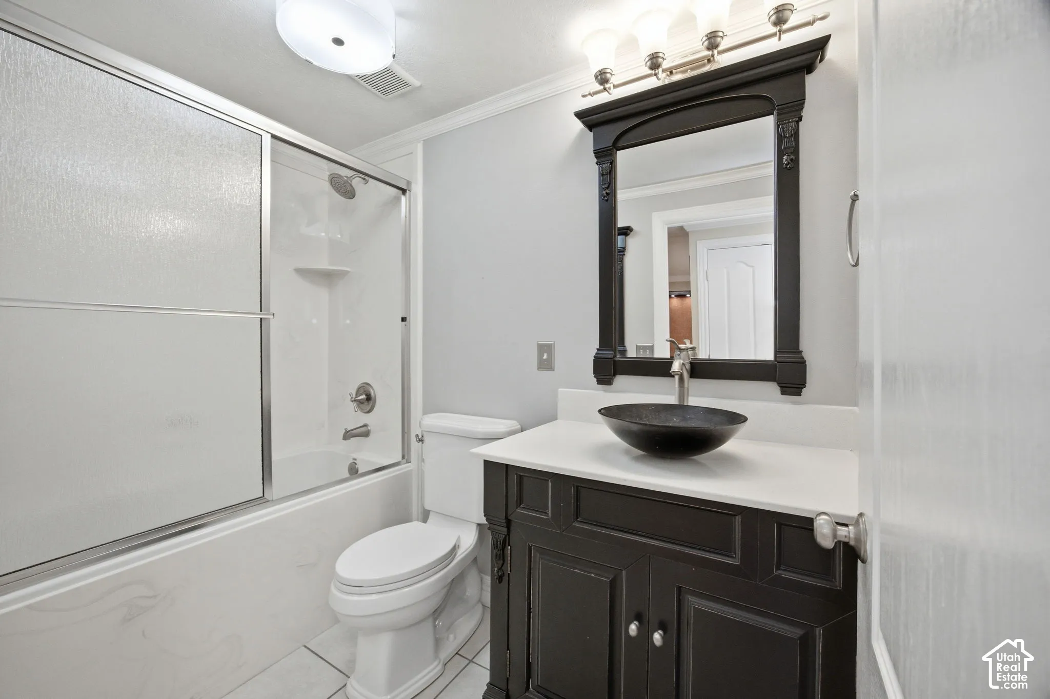 Bathroom featuring a dark-finish vanity with a light-toned countertop, a black vessel sink, a coordinating wall-mounted mirror, and a shower-tub combination with a glass sliding enclosure