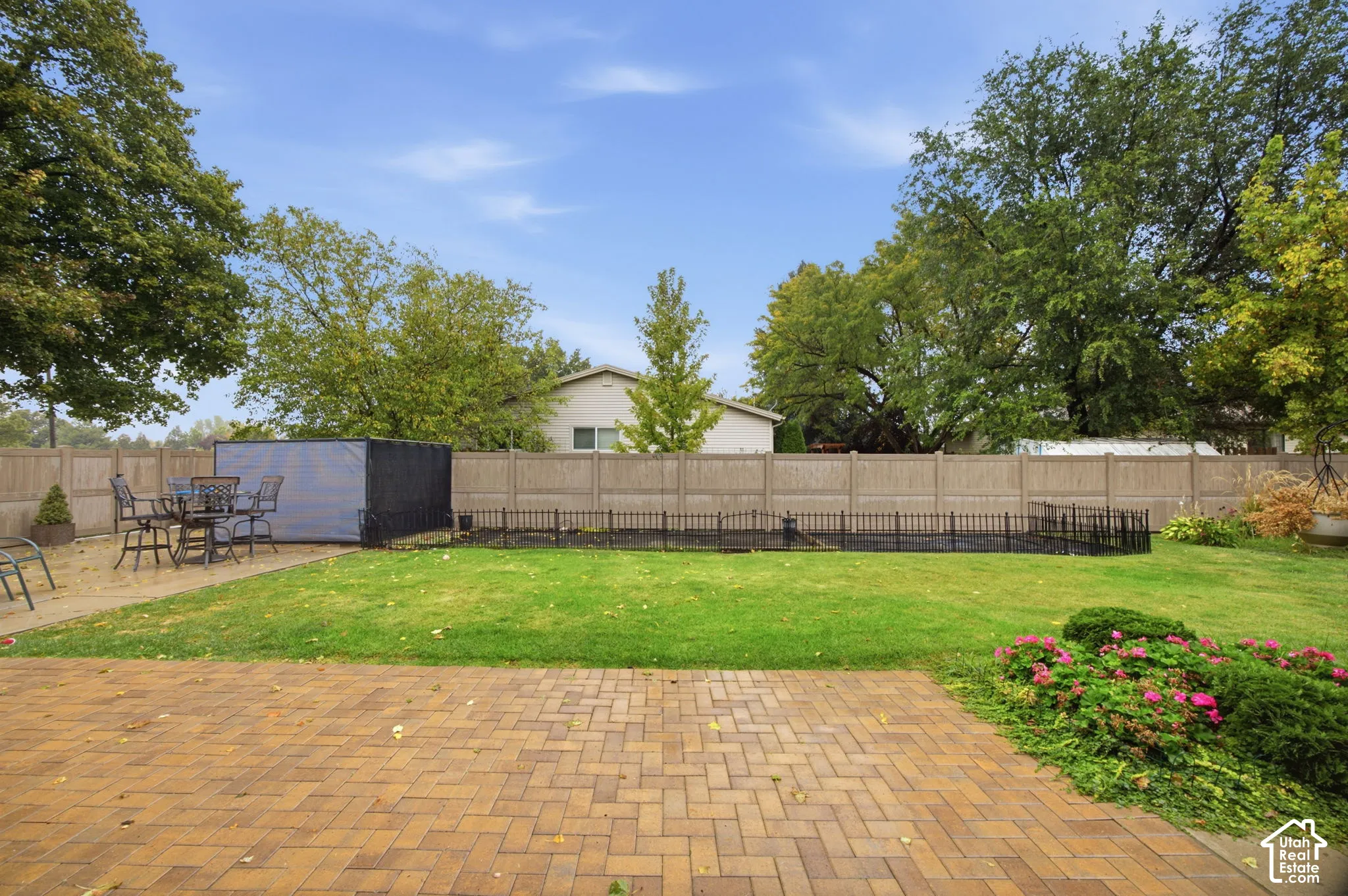 Backyard featuring a brick-paver patio, manicured lawn, established landscaping with flowering perennials, and a perimeter privacy fence