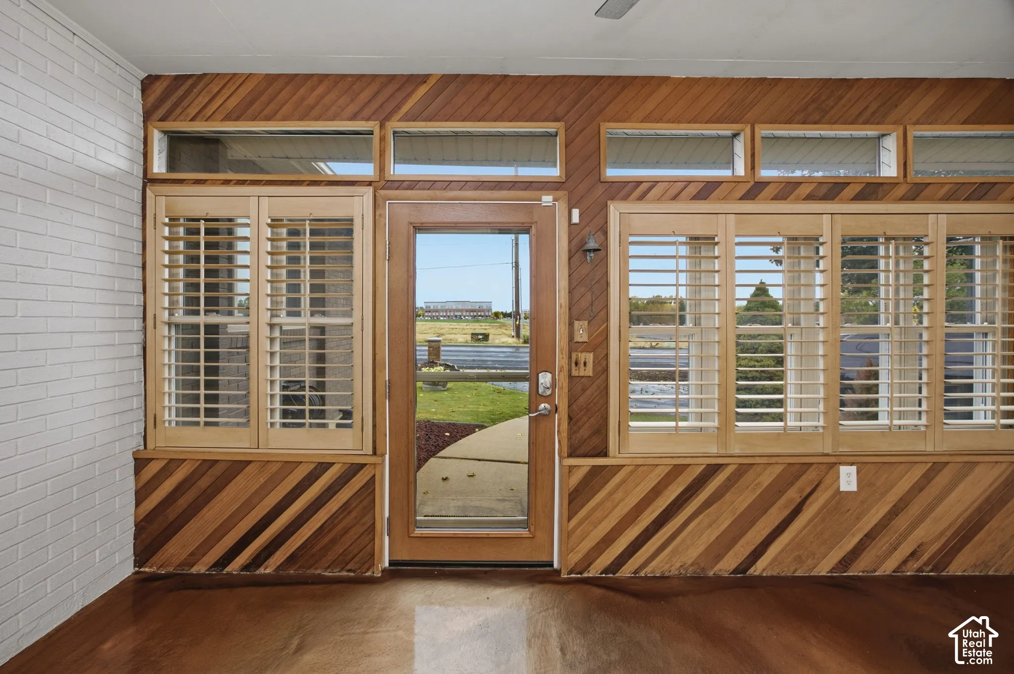 Diagonal wood paneling, white painted brick wall, polished concrete flooring, transom windows, and louvered wood shutters