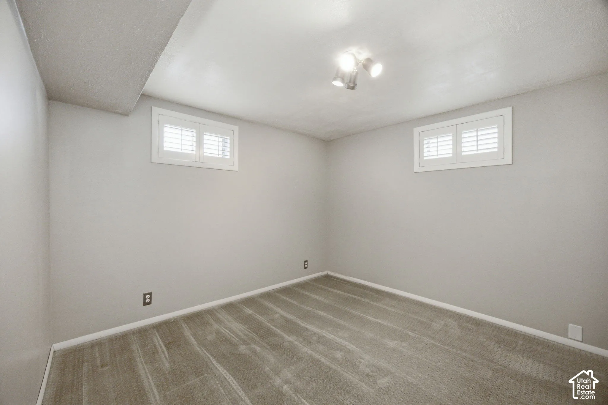 Bedroom #3 Neutral wall paint, plush carpeting, two windows with white shutter-style coverings, and three-bulb flush-mount ceiling light fixture