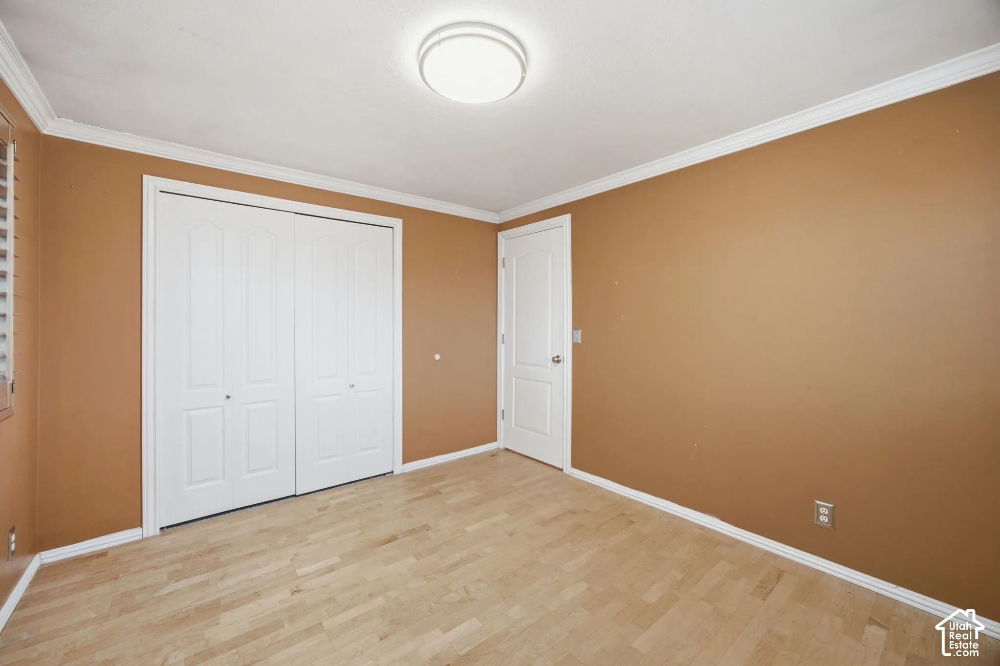 Bedroom #2 featuring wood-finish flooring, white crown molding, dual-panel closet doors, and a central flush-mount ceiling light