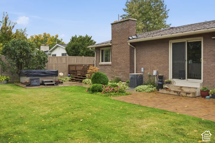 Brick exterior residence featuring a brick chimney, paved patio, raised wood deck, and fenced backyard