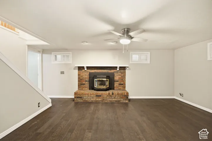 Brick fireplace with hearth and wood-burning stove insert, wood-finish flooring, and ceiling fan with integrated lighting
