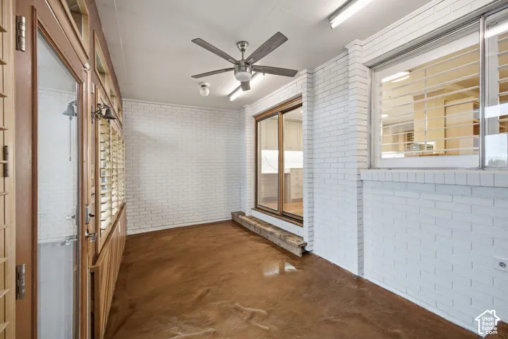 Enclosed porch featuring white painted brick walls, polished concrete flooring, wood-framed windows, and a ceiling fan with integrated lighting