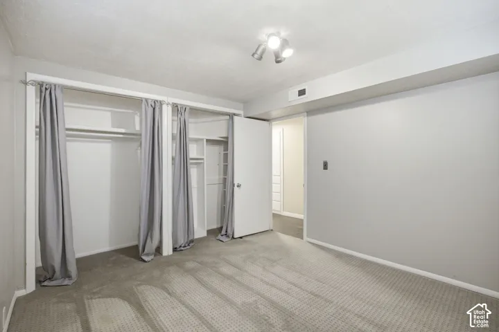 Bedroom #3 featuring wall-to-wall carpeting, triple-section reach-in closet with built-in shelving, white swing door, and three-bulb track lighting