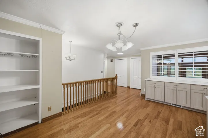 Interior space featuring wood-finish flooring, white built-in shelving, custom cabinetry with a solid surface countertop, louvered window shutters, and wood-railing staircase balustrade